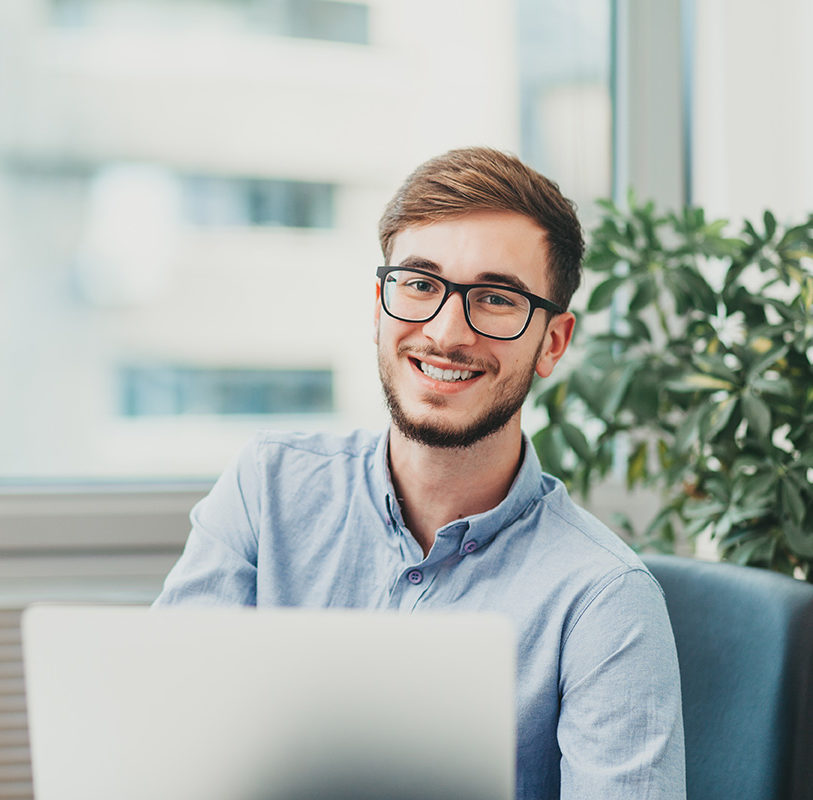 Young,Male,Intern,With,Glasses,Working,On,Laptop,And,Smiling